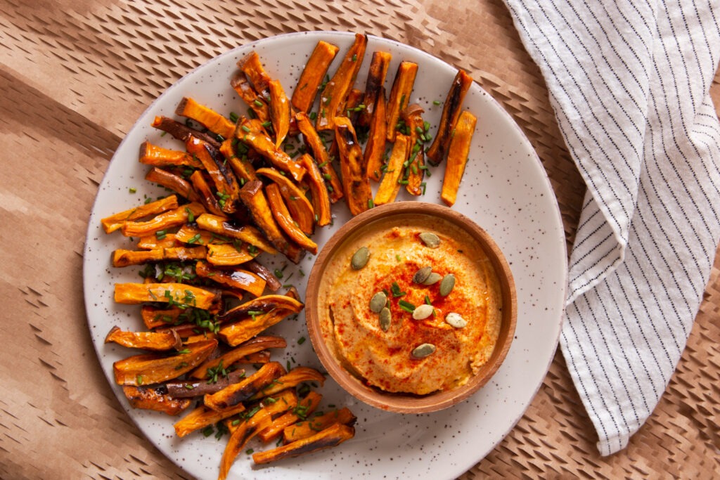 Butternut-Kürbis-Pommes mit Parmesan und KräuternBeschreibung: Frisch gebackene Butternut-Kürbis-Pommes, gewürzt mit Paprika und Knoblauch, garniert mit Petersilie und Parmesan, auf einem rustikalen Teller serviert.