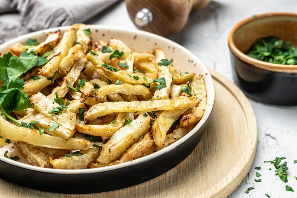 Pastinaken-Pommes mit Dip und KräuternBeschreibung: Knusprige Pastinaken-Pommes, goldbraun gebacken, mit einer würzigen Parmesan-Kruste und einem frischen Joghurt-Dip serviert.